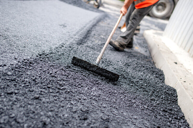 Man levelling permanent asphalt on road building